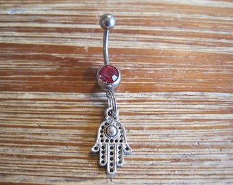 May include: Silver belly button ring with a red gem and a dangling charm shaped like a hamsa hand.