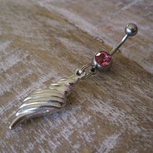 Puede incluir: Un charm de joyería corporal de plata con una gema rosa y un diseño de concha.