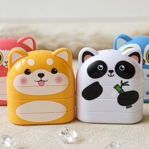 May include: Four colorful stackable pencil sharpeners with animal faces. The sharpeners are pink, yellow, white, and blue. The animals are a cat, a dog, a panda, and an owl.