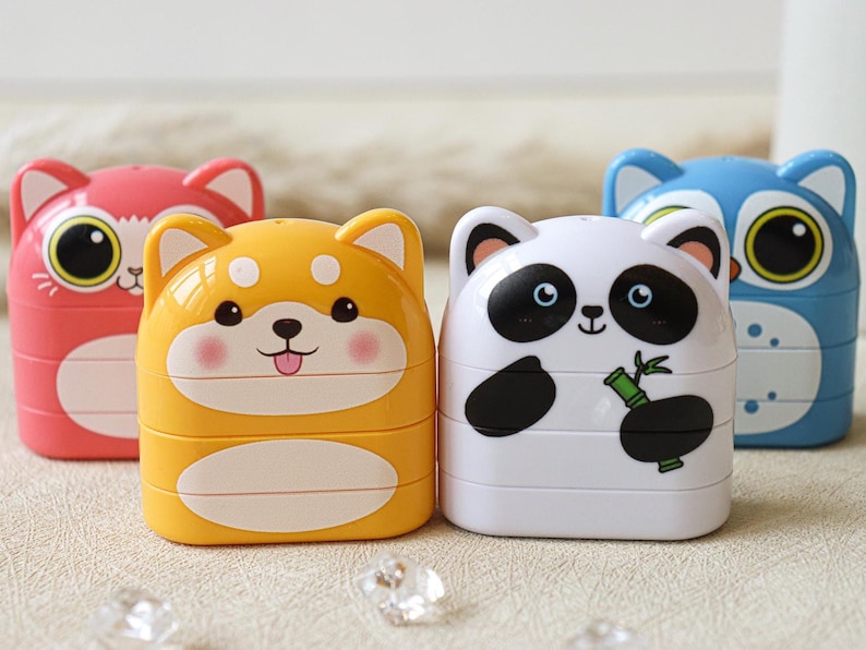 May include: Four colorful stackable pencil sharpeners with animal faces. The sharpeners are pink, yellow, white, and blue. The animals are a cat, a dog, a panda, and an owl.