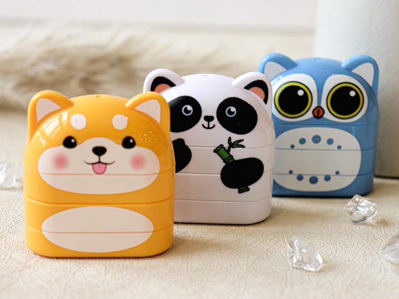 May include: Three colorful stackable pencil holders with animal designs. The first is a yellow Shiba Inu, the second is a white panda with a bamboo shoot, and the third is a blue owl.