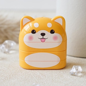 May include: A yellow plastic container shaped like a dog with a white face and pink cheeks. The container has a white oval on the bottom and is stacked on top of another container.