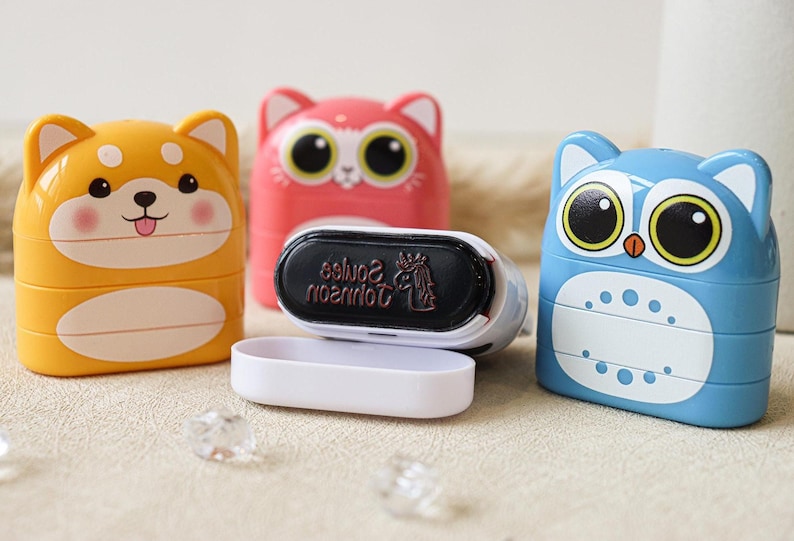 May include: Three colorful, stackable, self-inking stamps with animal designs. The stamps are yellow with a dog face, pink with a cat face, and blue with an owl face. The stamps are open, revealing the black ink pad with the text "Johnson Souvenirs" in red.