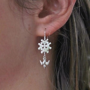 Könnte beinhalten: Silberne Ohrringe mit einem Schneeflocken-Design und einem Tauben-Anhänger.