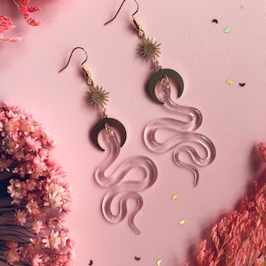 Peut inclure: Une paire de boucles d'oreilles en or avec un charme de serpent transparent et un charme de croissant de lune et d'étoile en or.