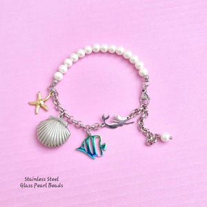 May include: A silver bracelet with a mermaid, starfish, seashell, and fish charm. The bracelet is made of stainless steel and glass pearl beads.