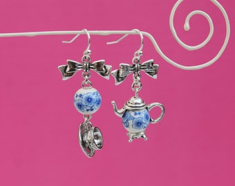 May include: Silver earrings with blue and white porcelain teacup and teapot charms. The charms are attached to silver bows.