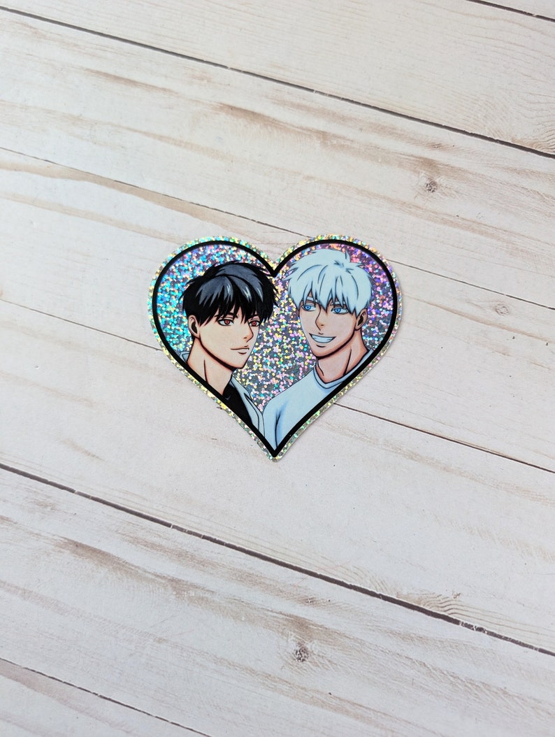 May include: A heart-shaped sticker with a glittery background featuring two anime characters. The character on the left has black hair and the character on the right has white hair.