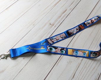 May include: A blue lanyard with a gold key design and a repeating pattern of anime eyes. The lanyard has a silver swivel clip.