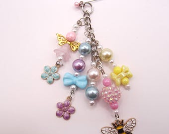 May include: A decorative brooch featuring a silver-tone pin base with multiple dangling charms including a bee, flowers, a bow, and various colorful beads in shades of pink, blue, yellow, and purple, arranged on silver-tone metal chains.