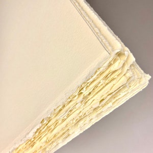 K&ouml;nnte beinhalten: Nahaufnahme der Kante eines Stapels handgemachtem Papiers. Das Papier ist hellgelb und hat eine raue, strukturierte Oberfl&auml;che.