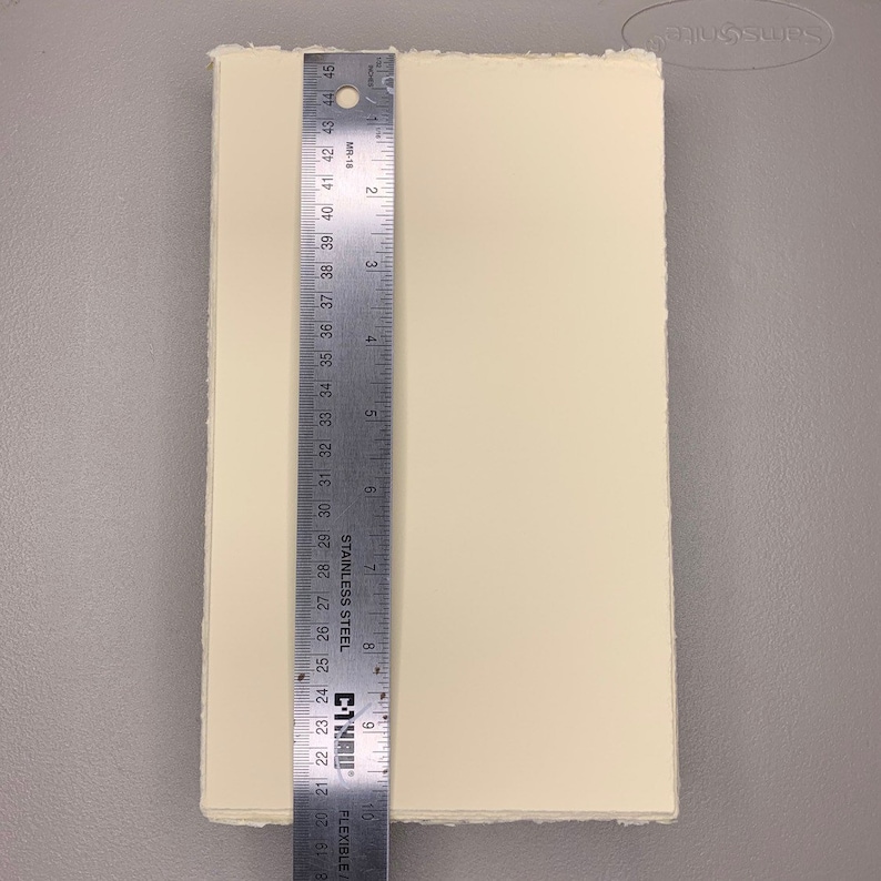 K&ouml;nnte beinhalten: Nahaufnahme eines Blattes cremefarbenen Papiers mit leicht strukturierter Oberfl&auml;che. Das Papier wird mit einem Lineal gemessen und zeigt, dass es etwa 23 cm x 30 cm gro&szlig; ist.