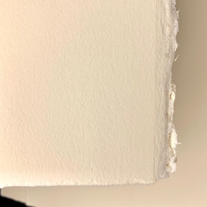 K&ouml;nnte beinhalten: Nahaufnahme eines Blattes wei&szlig;en handgesch&ouml;pften Papiers mit einer rauen, strukturierten Oberfl&auml;che. Die Kanten des Papiers sind uneben und leicht ausgefranst.