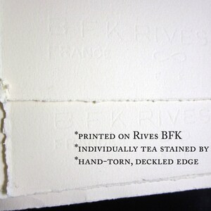 May include: Close-up of the edge of a white paper sheet with a deckled edge. The paper is printed with the text "*PRINTED ON RIVES BFK *INDIVIDUALLY TEA STAINED BY HAND *HAND-TORN, DECKLED EDGE".