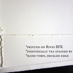 May include: Close-up of the edge of a sheet of white paper with a deckled edge. The paper is printed with the text "*PRINTED ON RIVES BFK *INDIVIDUALLY TEA STAINED BY HAND *HAND-TORN, DECKLED EDGE"