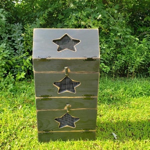 May include: A three-tier compost bin made of wood with a dark green stain. Each tier has a star-shaped opening with a wire mesh insert. The bin is sitting on a bed of green grass.