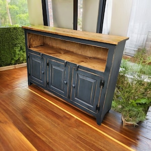 May include: A dark blue wooden cabinet with three doors and a shelf. The cabinet has black hinges and knobs. The cabinet is sitting on a wooden floor.