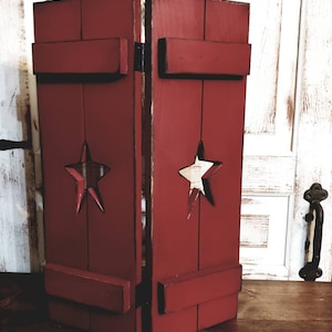 May include: A rustic, red wooden decorative box with a distressed finish. The box features a star cut-out design and is hinged, suggesting it can open. The box is likely for storage or display.