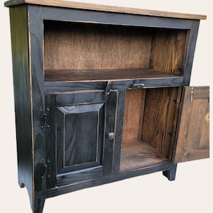 A black wooden cabinet with a single door and a shelf. The door is open and the shelf is empty. The cabinet has a distressed finish and is made of solid wood.