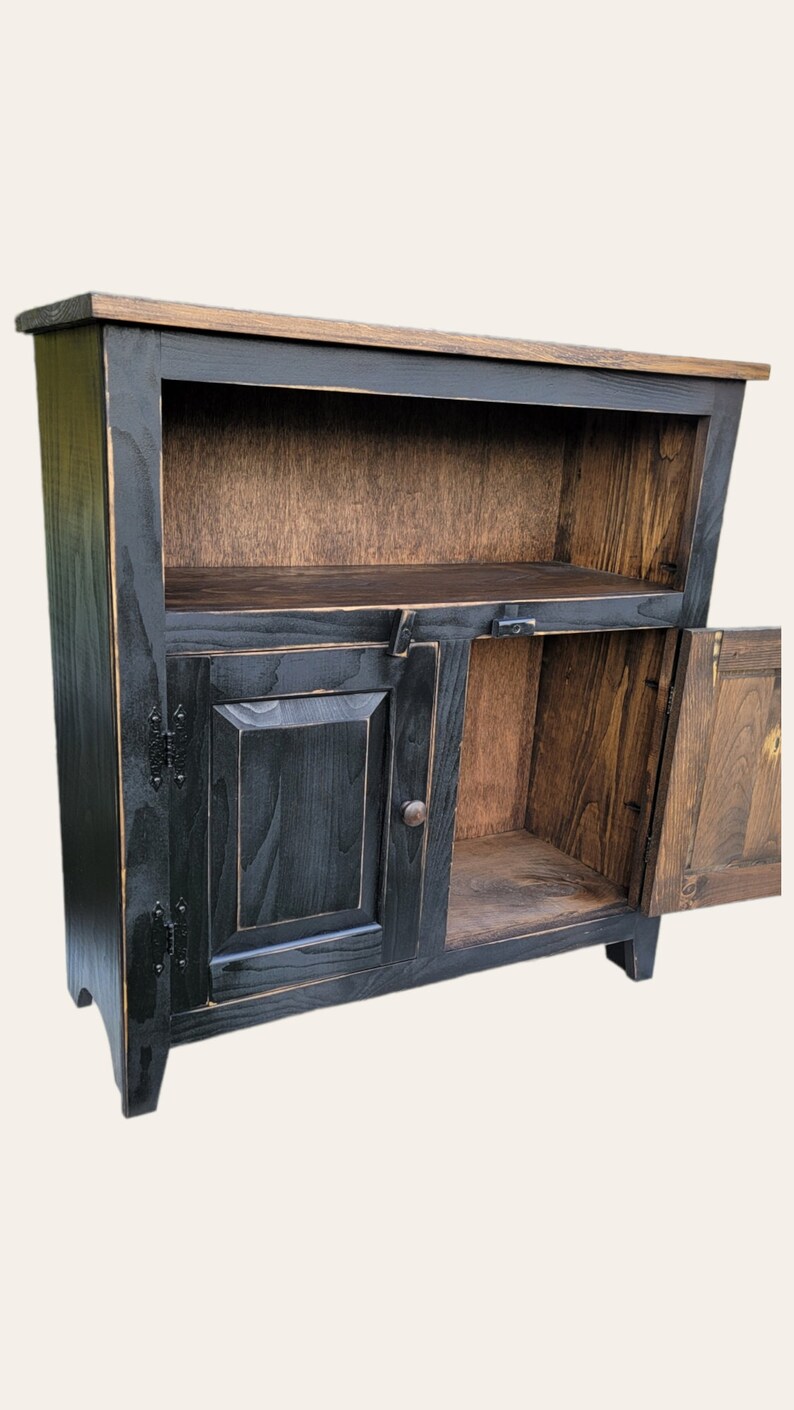 A black wooden cabinet with a single door and a shelf. The door is open and the shelf is empty. The cabinet has a distressed finish and is made of solid wood.