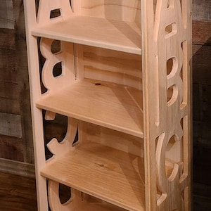 May include: A light-colored wooden bookshelf with four shelves. The sides of the bookshelf are cut out in the shape of the letters A, B, C, and D. The bookshelf is made of unfinished wood.
