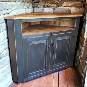 May include: A black corner cabinet with two doors and a wooden top and shelf. The cabinet is made of wood and has a distressed finish. The cabinet is designed to fit into a corner and has a rustic style.