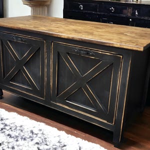 May include: A black cabinet with a distressed finish and a natural wood top. The cabinet doors feature an X-shaped design. The cabinet has a rectangular shape and is likely used for storage.