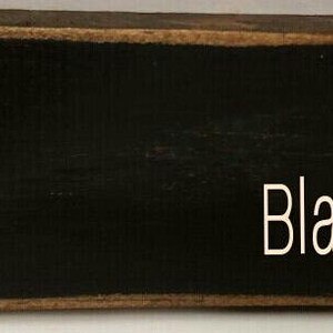 A black wooden sign with the word 'Black' written in white paint.