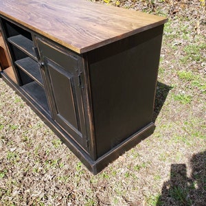 A black wooden media console with a wood top and two doors. The console has shelves for storage and a distressed finish.
