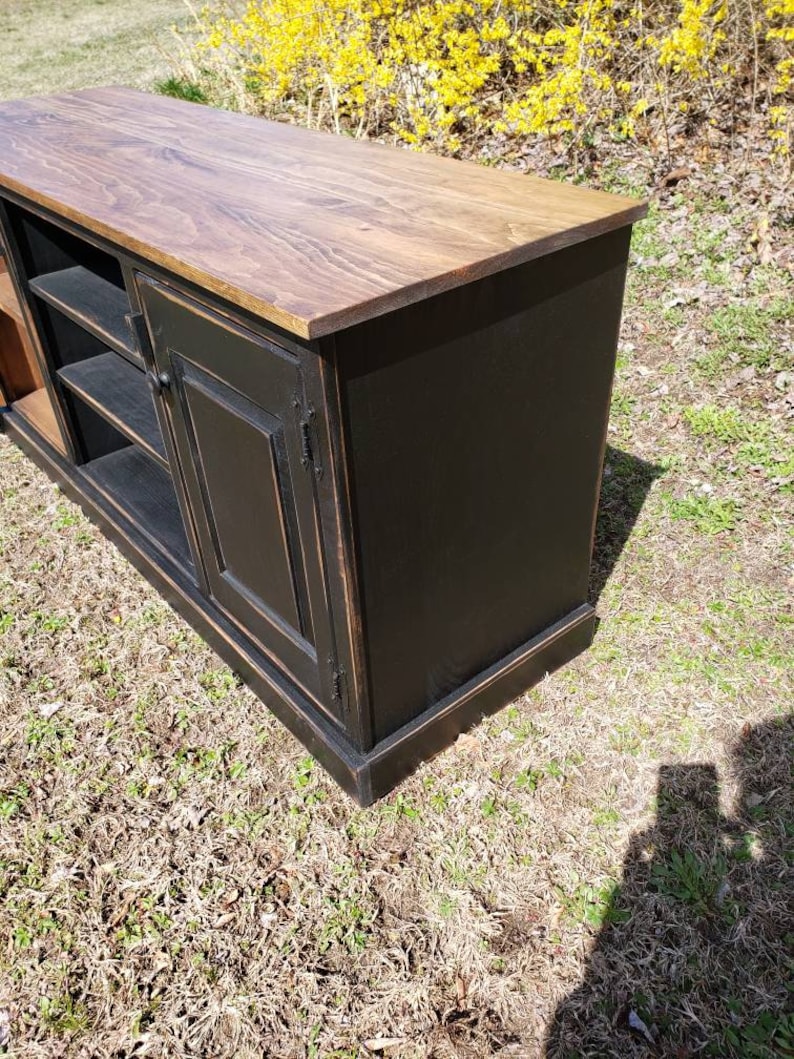 A black wooden media console with a wood top and two doors. The console has shelves for storage and a distressed finish.