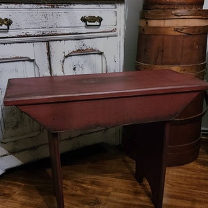 May include: A small, antique red table with a rectangular top and angled legs. The table is made of wood and has a distressed finish. The table is approximately 30 inches long and 18 inches wide, perfect for a living room or entryway.