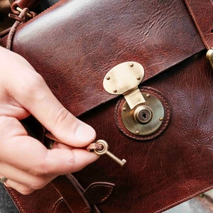 May include: A brown leather briefcase with a brass lock and key. The briefcase has a strap and a handle.