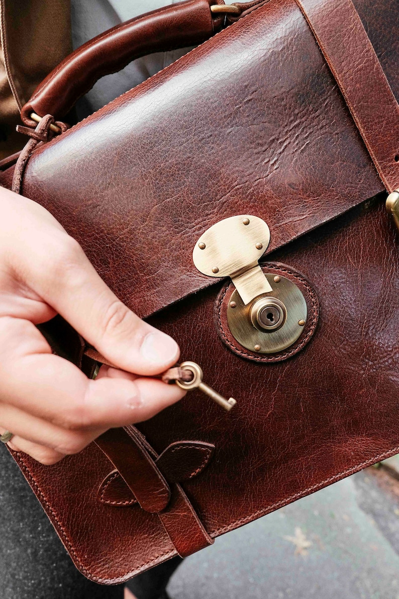 May include: A brown leather briefcase with a brass lock and key. The briefcase has a strap and a handle.