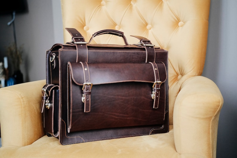 May include: A brown leather briefcase with multiple pockets and buckles. The briefcase is sitting on a yellow armchair.