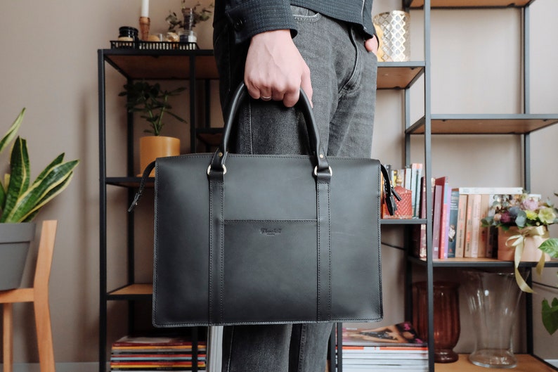May include: A black leather briefcase with a gold zipper and a small pocket on the front. The briefcase has a handle and a strap.