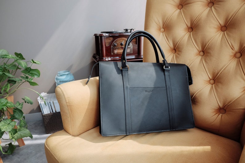 May include: A black leather briefcase with a top handle and a small pocket on the front. The briefcase is sitting on a yellow armchair.