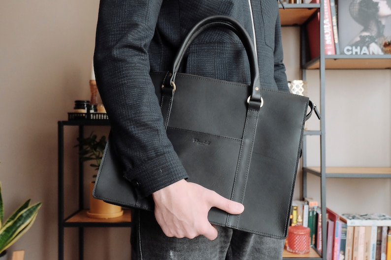 May include: A black leather briefcase with a top handle and a zippered closure. The briefcase has a subtle embossed logo on the front.