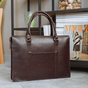 May include: A brown leather briefcase with a zipper and two handles. The briefcase is sitting on a wooden floor.