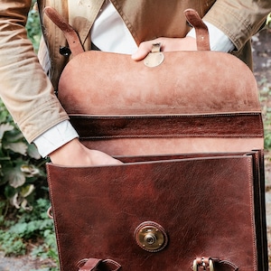 May include: A brown leather briefcase with a flap closure and brass hardware. The briefcase has a single strap and is open to reveal a brown leather interior.