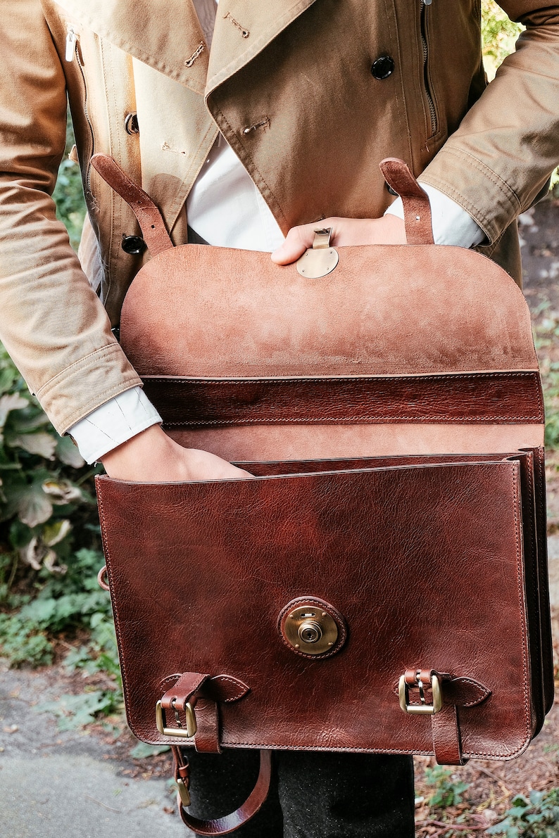 May include: A brown leather briefcase with a flap closure and brass hardware. The briefcase has a single strap and is open to reveal a brown leather interior.