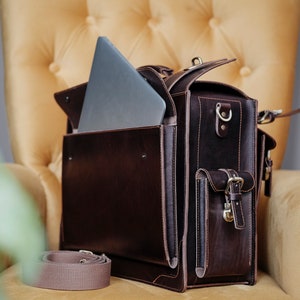 May include: A brown leather briefcase with a laptop inside and a separate strap. The briefcase has a flap with a buckle and a pocket on the front.