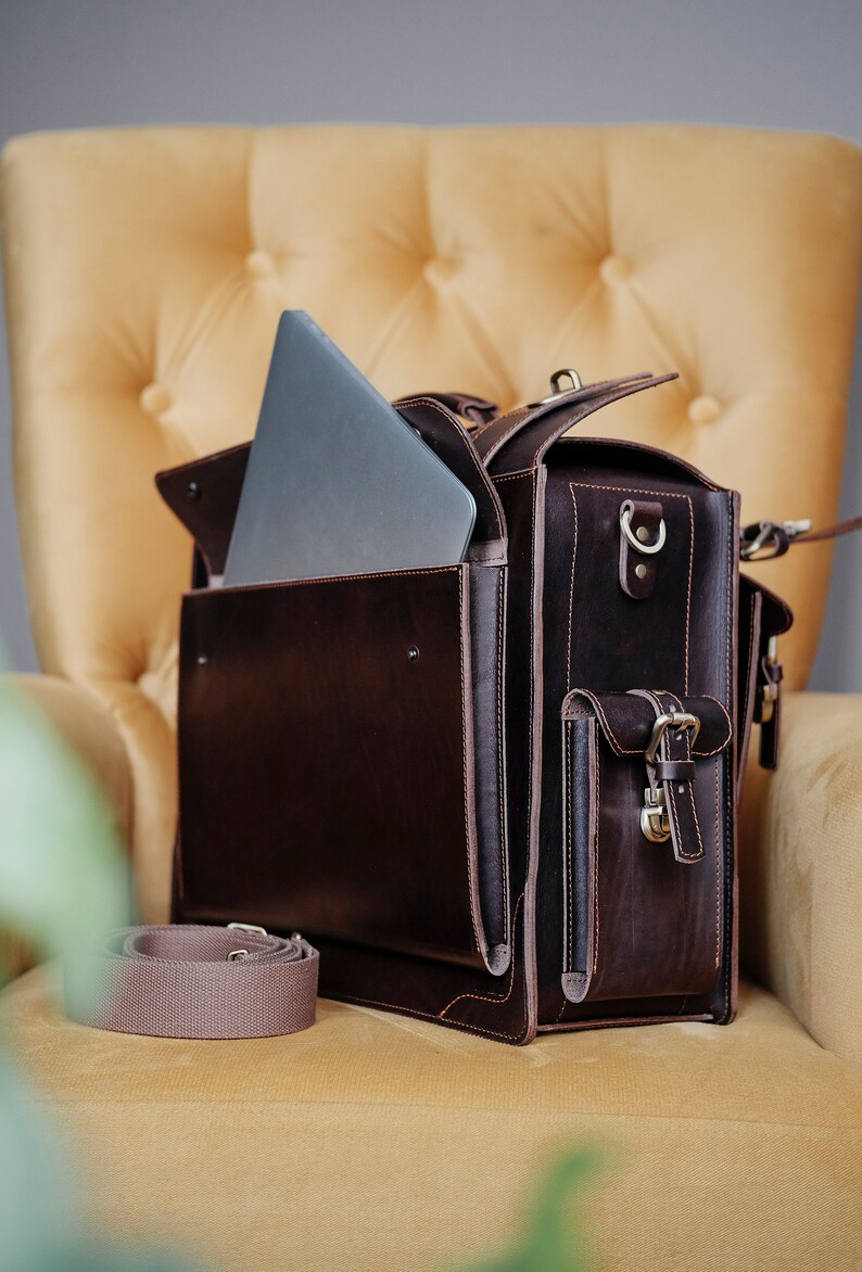 May include: A brown leather briefcase with a laptop inside and a separate strap. The briefcase has a flap with a buckle and a pocket on the front.