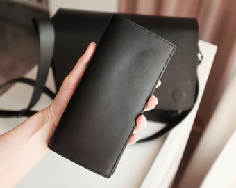 May include: A black leather wallet with a stitched edge. The wallet is being held in a hand.