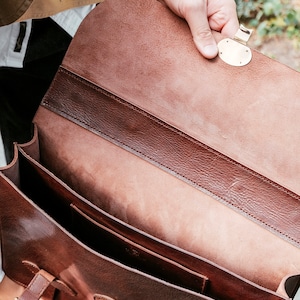 May include: A brown leather briefcase with a brass clasp and buckle. The briefcase is open and the inside is lined with brown leather.