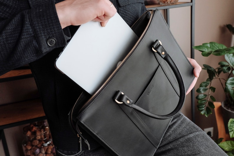 May include: A black leather briefcase with a gold zipper and a gold buckle. A laptop computer is being placed inside the briefcase.