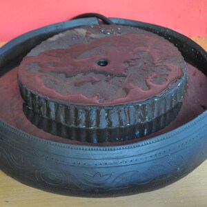 May include: A black ceramic fountain with a round, textured top. The fountain is filled with water and has a small hole in the centre of the top.