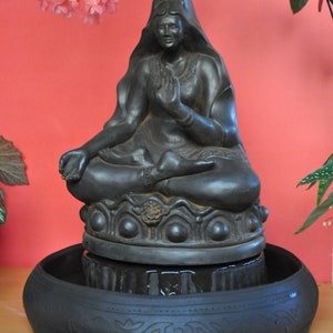 May include: Black ceramic fountain featuring a seated Buddha statue with a serene expression. The fountain has a circular base with intricate details and a water basin.
