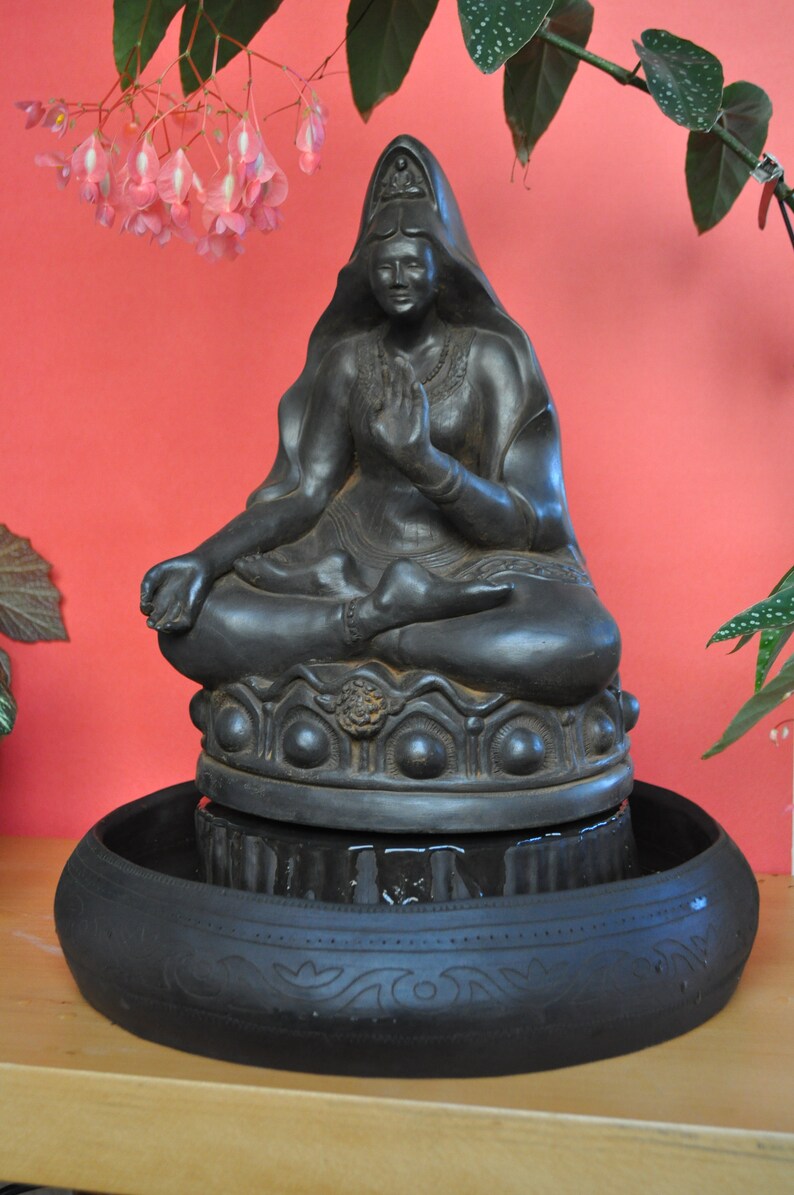 May include: Black ceramic fountain featuring a seated Buddha statue with a serene expression. The fountain has a circular base with intricate details and a water basin.