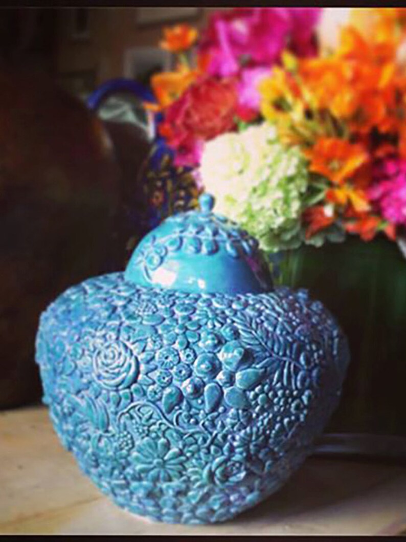 K&ouml;nnte beinhalten: Eine tealblaue Keramikvase mit floralem Muster. Die Vase ist mit einem erhabenen Blumenmuster verziert und hat eine abgerundete Form.
