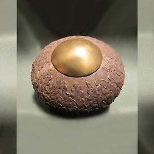 May include: A round, brown, ceramic box with a gold lid. The box is decorated with a raised design of leaves and flowers.